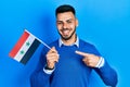 Young hispanic man with beard holding syria flag smiling happy pointing with hand and finger Royalty Free Stock Photo