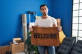 Young hispanic man with beard holding welcome doormat at new home afraid and shocked with surprise and amazed expression, fear and Royalty Free Stock Photo