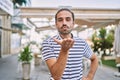 Young hispanic man with beard outdoors at the city looking at the camera blowing a kiss with hand on air being lovely and sexy Royalty Free Stock Photo