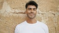 A young hispanic man with a beard poses confidently in front of an isolated brown brick wall, looking approachable and casual Royalty Free Stock Photo