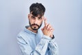 Young hispanic man with beard standing over blue background holding symbolic gun with hand gesture, playing killing shooting