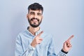 Young hispanic man with beard standing over blue background smiling and looking at the camera pointing with two hands and fingers Royalty Free Stock Photo