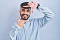 Young hispanic man with beard standing over blue background smiling making frame with hands and fingers with happy face Royalty Free Stock Photo