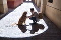 Young Hispanic man with beard and sunglasses crouching with his dog holding his paw on a sunny street at sunset casting his shadow Royalty Free Stock Photo