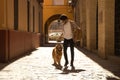 Young Hispanic man with beard and sunglasses with his dog holding on to the leash walking along a sunny street at sunset. Concept Royalty Free Stock Photo