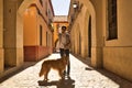 Young Hispanic man with beard and sunglasses waving goodbye to camera with his dog holding on to leash walking along a sunny Royalty Free Stock Photo