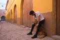 Young Hispanic man with beard, sunglasses and white shirt, leaning against a wall hugging his dog between his legs. Concept Royalty Free Stock Photo