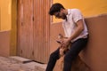 Young Hispanic man with beard, sunglasses and white shirt, leaning against a wall hugging his dog between his legs. Concept Royalty Free Stock Photo