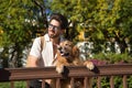 Young Hispanic man with beard, sunglasses and white shirt, leaning out with his dog leaning on a railing in funny attitude. Royalty Free Stock Photo