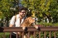 Young Hispanic man with beard, sunglasses and white shirt, leaning out with his dog leaning on a railing in funny attitude. Royalty Free Stock Photo