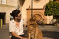 Young Hispanic man with beard, sunglasses and white shirt, sitting on a bench hugging and petting his dog. Concept animals, dogs, Royalty Free Stock Photo