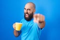 Young hispanic man with beard and tattoos drinking a cup of coffee pointing displeased and frustrated to the camera, angry and Royalty Free Stock Photo