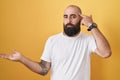 Young hispanic man with beard and tattoos standing over yellow background confused and annoyed with open palm showing copy space