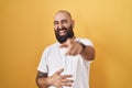 Young hispanic man with beard and tattoos standing over yellow background laughing at you, pointing finger to the camera with hand Royalty Free Stock Photo