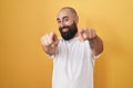 Young hispanic man with beard and tattoos standing over yellow background pointing to you and the camera with fingers, smiling Royalty Free Stock Photo