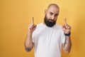 Young hispanic man with beard and tattoos standing over yellow background pointing up looking sad and upset, indicating direction Royalty Free Stock Photo