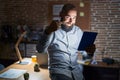 Young hispanic man with beard and tattoos working at the office at night beckoning come here gesture with hand inviting welcoming Royalty Free Stock Photo