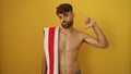 Young hispanic man with beard and towel giving thumb down isolated over yellow background Royalty Free Stock Photo