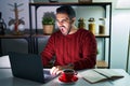 Young hispanic man with beard using computer laptop at night at home angry and mad screaming frustrated and furious, shouting with Royalty Free Stock Photo