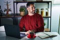 Young hispanic man with beard using computer laptop at night at home looking to side, relax profile pose with natural face and Royalty Free Stock Photo