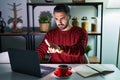 Young hispanic man with beard using computer laptop at night at home pointing with finger up and angry expression, showing no Royalty Free Stock Photo