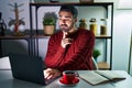Young hispanic man with beard using computer laptop at night at home thinking concentrated about doubt with finger on chin and Royalty Free Stock Photo