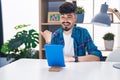 Young hispanic man with beard using touchpad sitting on the table pointing thumb up to the side smiling happy with open mouth Royalty Free Stock Photo