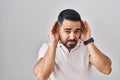 Young hispanic man with beard wearing casual clothes over white background trying to hear both hands on ear gesture, curious for Royalty Free Stock Photo