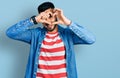 Young hispanic man with beard wearing casual denim jacket doing heart shape with hand and fingers smiling looking through sign Royalty Free Stock Photo