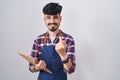 Young hispanic man with beard wearing waiter apron holding clipboard beckoning come here gesture with hand inviting welcoming Royalty Free Stock Photo