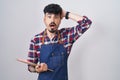 Young hispanic man with beard wearing waiter apron holding clipboard crazy and scared with hands on head, afraid and surprised of Royalty Free Stock Photo