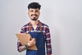 Young hispanic man with beard wearing waiter apron holding clipboard with a happy and cool smile on face