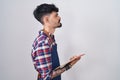 Young hispanic man with beard wearing waiter apron holding clipboard looking to side, relax profile pose with natural face and