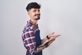 Young hispanic man with beard wearing waiter apron holding clipboard pointing aside with hands open palms showing copy space, Royalty Free Stock Photo