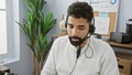 A young hispanic man with a beard working indoors at an office wearing a headset Royalty Free Stock Photo