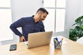 Young hispanic man with beard working at the office with laptop suffering of backache, touching back with hand, muscular pain Royalty Free Stock Photo