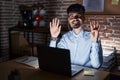 Young hispanic man with beard working at the office at night showing and pointing up with fingers number nine while smiling