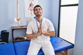 Young hispanic man with beard working at pain recovery clinic begging and praying with hands together with hope expression on face Royalty Free Stock Photo