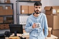 Young hispanic man with beard working at small business ecommerce drinking from boss cup thinking attitude and sober expression Royalty Free Stock Photo