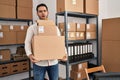 Young hispanic man with beard working at small business ecommerce holding delivery boxes in shock face, looking skeptical and Royalty Free Stock Photo
