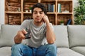 Young hispanic man bored watching tv sitting on the sofa at home