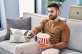 Young hispanic man boring watching movie sitting on sofa at home Royalty Free Stock Photo