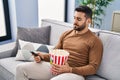 Young hispanic man boring watching movie sitting on sofa at home Royalty Free Stock Photo