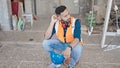 Young hispanic man builder sitting on the floor resting at construction site