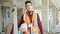 Young hispanic man builder standing with serious face holding hardhat at construction site Royalty Free Stock Photo