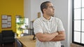 Young hispanic man business worker standing with relaxed expression and arms crossed gesture at office Royalty Free Stock Photo