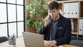 Young hispanic man business worker talking on the phone using laptop at office Royalty Free Stock Photo