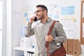 Young hispanic man business worker talking on smartphone holding briefcase at office Royalty Free Stock Photo