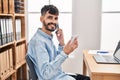 Young hispanic man business worker talking on smartphone reading notebook at office Royalty Free Stock Photo