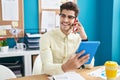Young hispanic man business worker talking on smartphone using touchpad at office Royalty Free Stock Photo